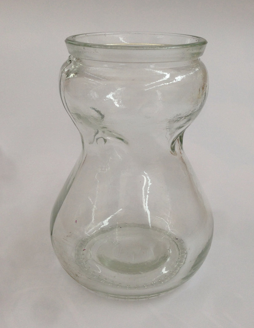 A clear, traditional hourglass-shaped glass hyacinth forcing carafe vase designed to hold a bulb above water for indoor root growth.