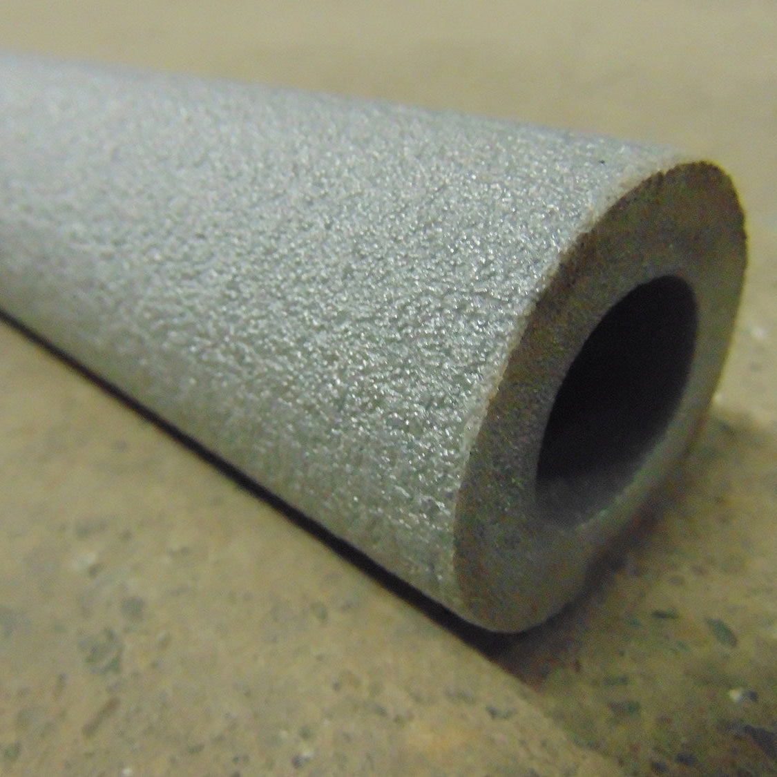 A rolled up piece of gray foam pipe insulation with a scored edge, placed on a flat surface.