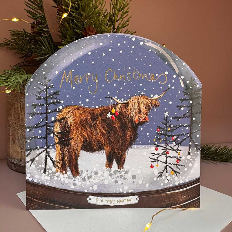 Alex Clark Highland Cow Snow Globe greeting card depicting a fluffy Scottish cow in a snowy globe with a white envelope.