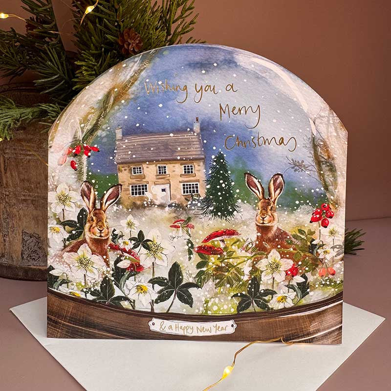 Alex Clark Christmas Hares Snow Globe greeting card depicting hares in a snowy landscape with a white envelope.