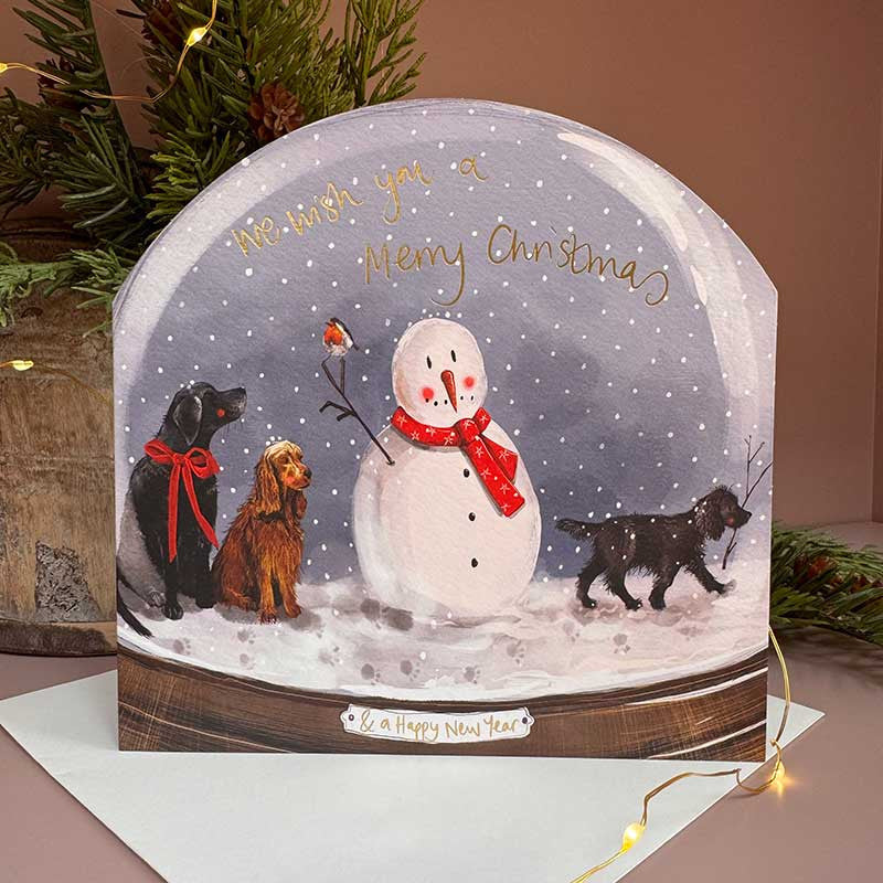 Alex Clark Dogs & Snowman Snow Globe greeting card depicting playful dogs around a snowman with a white envelope.
