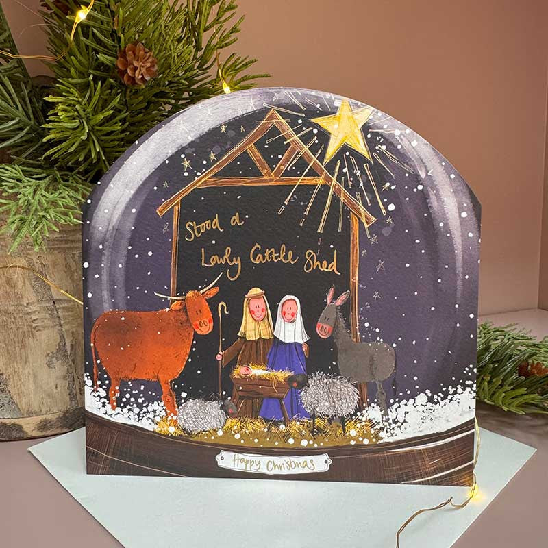 Alex Clark Nativity Snow Globe greeting card depicting Mary, Joseph, and baby Jesus in a snowy scene with a white envelope.