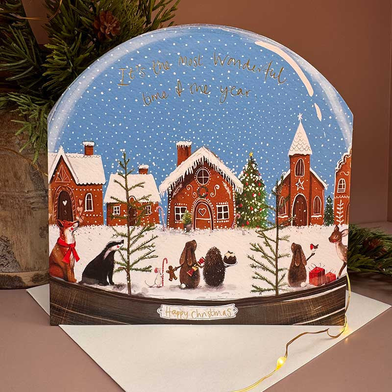 Alex Clark Gingerbread Village Snow Globe greeting card showing a sweet festive illustration with a white envelope.