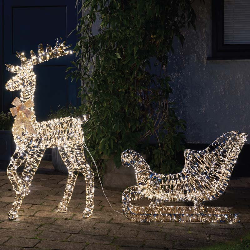 Smart Garden Gold Twist Reindeer & Sleigh lit up with warm white LEDs on a lawn at night.
