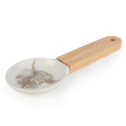 Candlelight Highland Cow spoon rest with glazed ceramic dish and natural wood handle resting on a wooden kitchen worktop