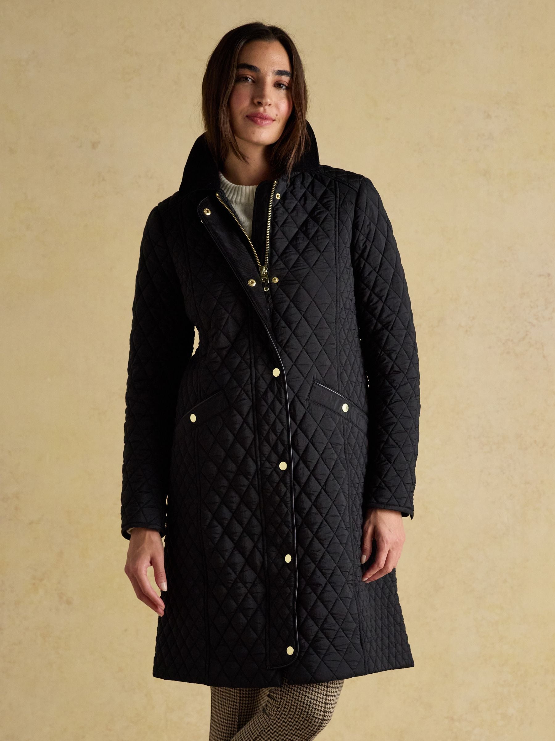 Women's black longline diamond quilted showerproof coat with a classic cord collar and welt pockets, shown from the front.