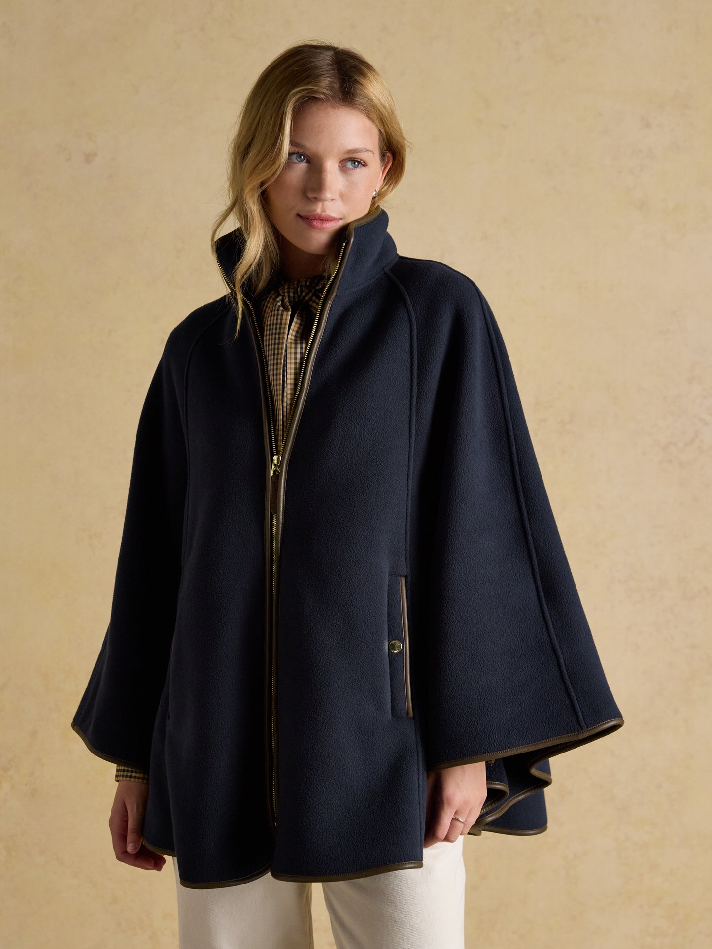 Woman wearing a navy Joules longline polar fleece cape with brown PU binding and a zipped front.
