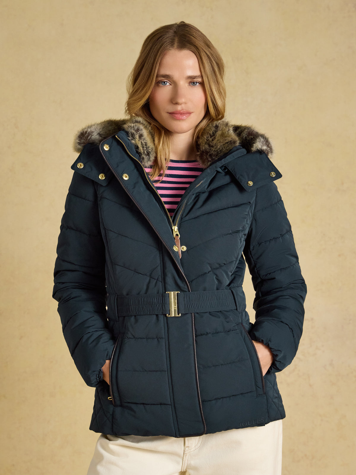 Joules Aspen women's showerproof padded coat in mid-thigh length with a belted waist and faux fur hood trim.