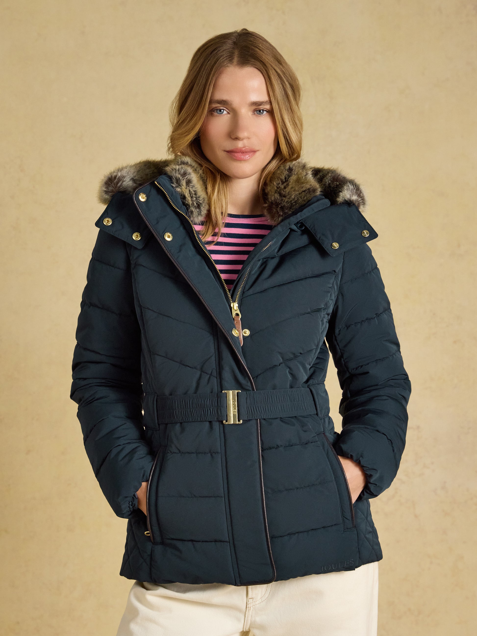 Joules Aspen women's showerproof padded coat in mid-thigh length with a belted waist and faux fur hood trim.
