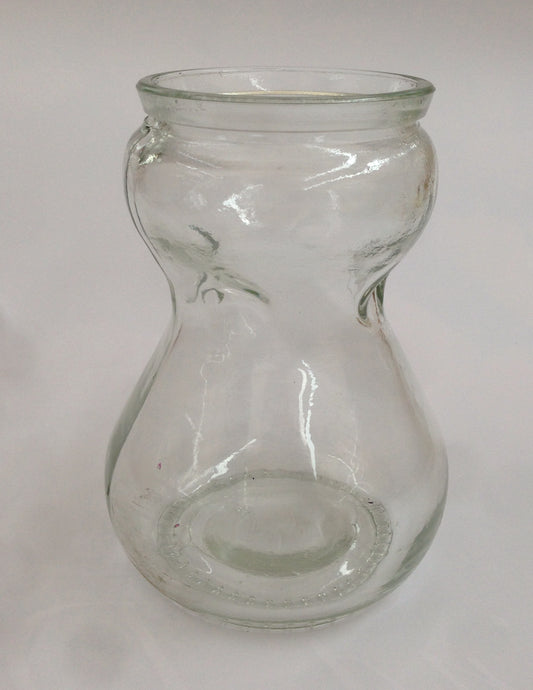 A clear, traditional hourglass-shaped glass hyacinth forcing carafe vase designed to hold a bulb above water for indoor root growth.