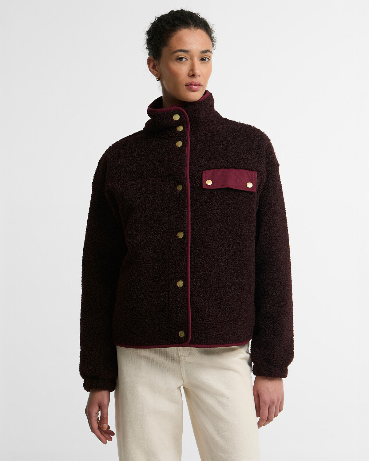 Woman wearing a deep burgundy Barbour Mabel button-up fleece bomber jacket with a high collar, contrasting red trim, and brass buttons.