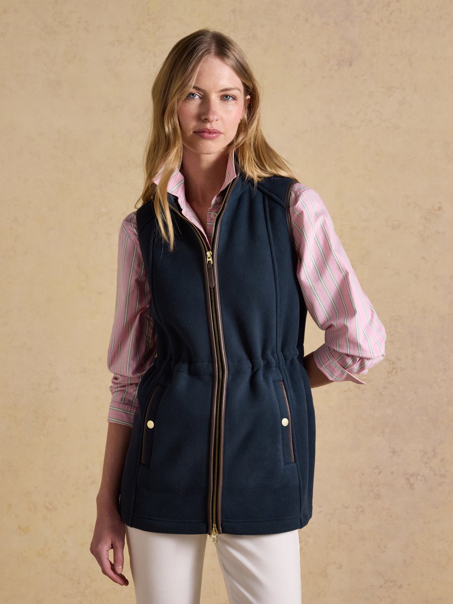 Woman wearing a navy Joules longline polar fleece gilet with faux leather trim over a striped top.
