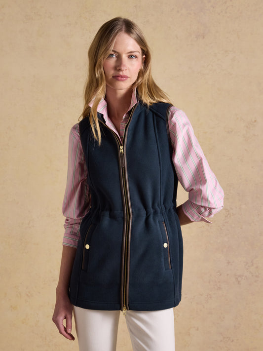 Woman wearing a navy Joules longline polar fleece gilet with faux leather trim over a striped top.