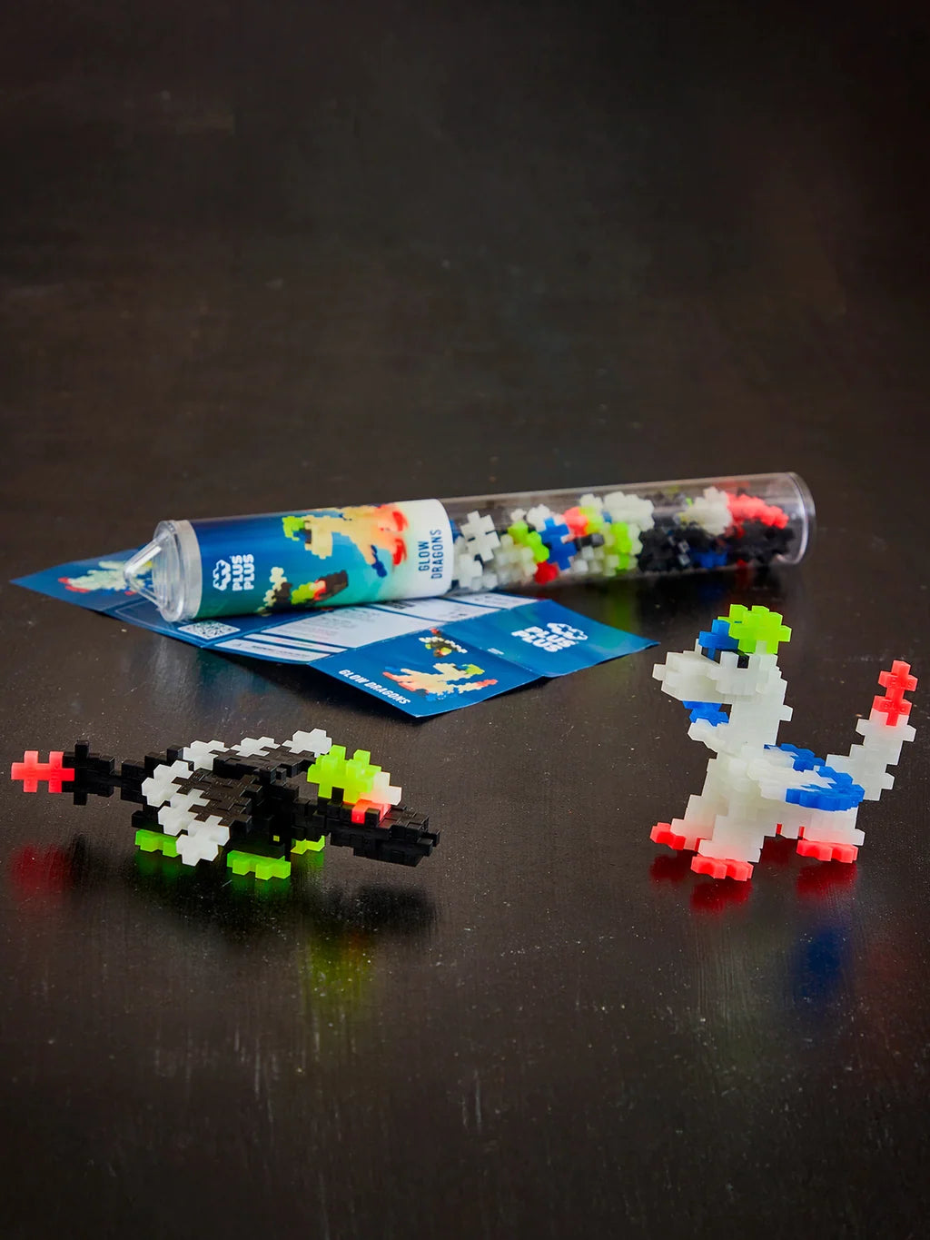 Plus-Plus Glow Dragons clear tube container displayed with built black and white glow-in-the-dark toy dragon figures.