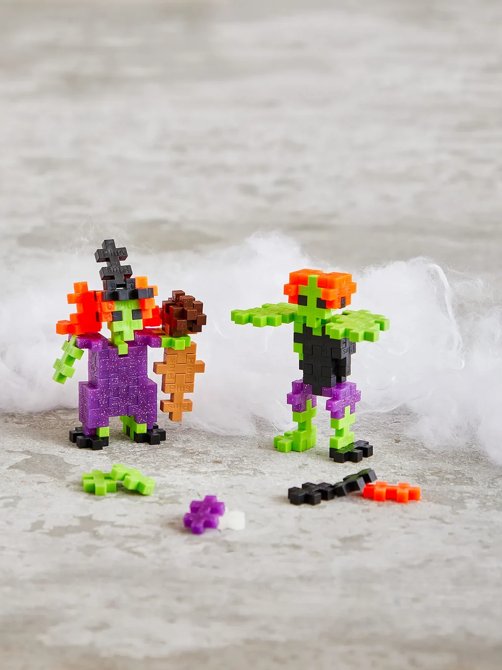 Plus-Plus Monster Mash tube packaged alongside two built monster figures in purple, green, and orange interlocking pieces.