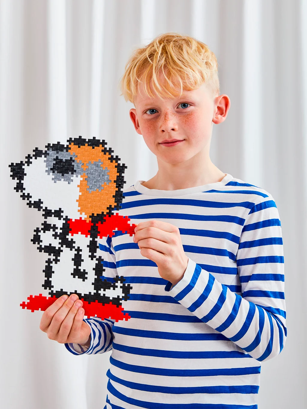 Plus-Plus Snoopy Flying Ace tube container alongside the assembled pixel-style Snoopy artwork featuring his aviator cap and red scarf.