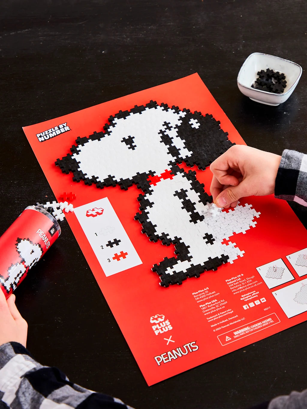 Plus-Plus Snoopy Puzzle by Number tube packaging beside a completed black and white Snoopy figure with a red collar.