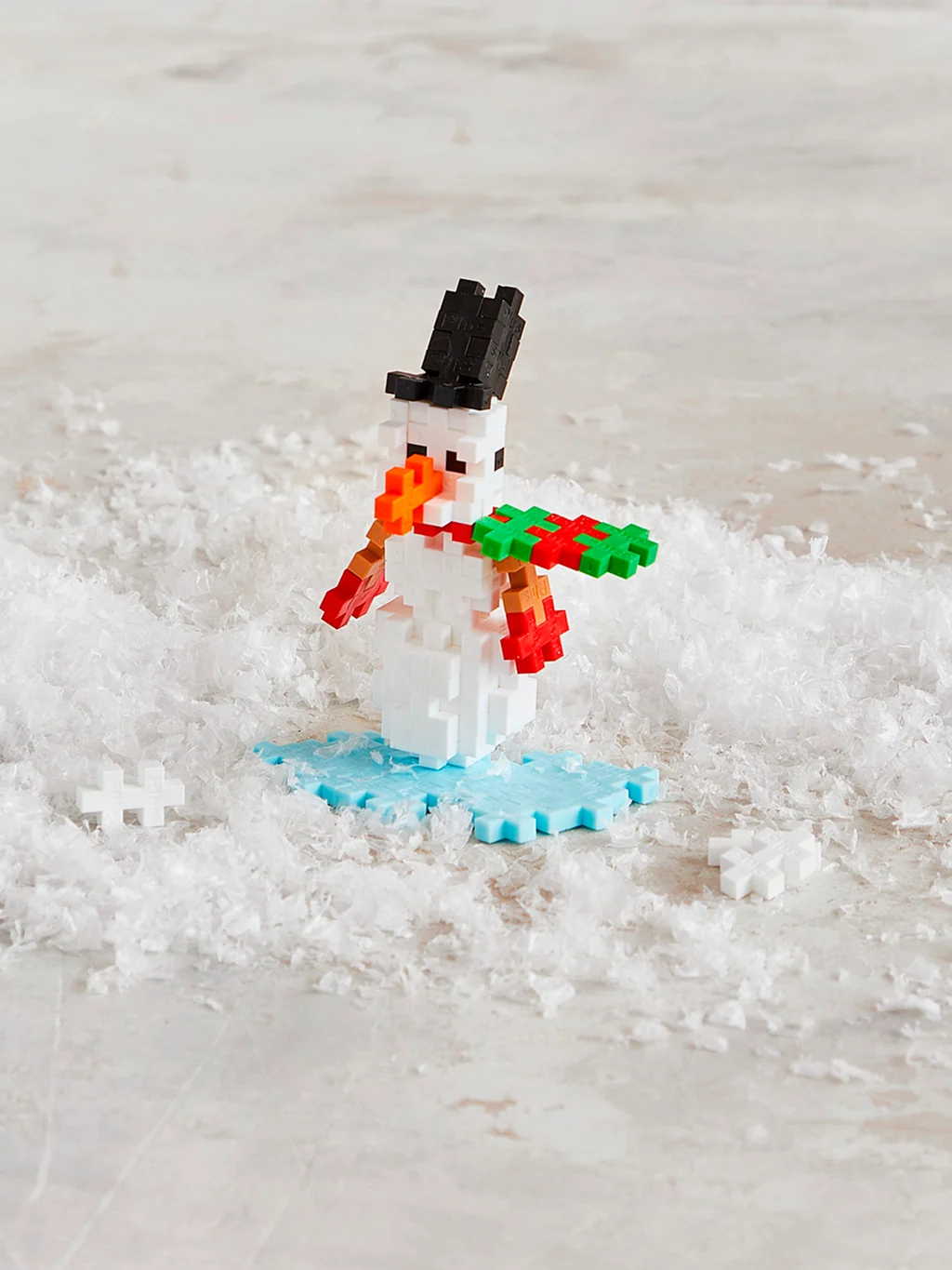 Plus-Plus Snowman storage tube displayed alongside a constructed snowman figure wearing a black hat, scarf, and red mittens.