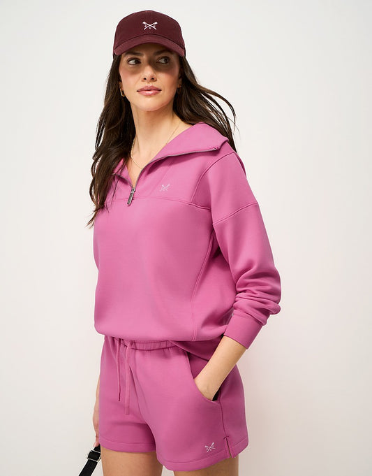 Woman wearing a vibrant orchid pink Crew Clothing SuperLuxe Half Zip Sweater featuring a broad collar, brushed metal zip, and printed crossed oars on the chest.