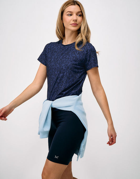 Front view of a woman wearing the navy abstract print Crew Clothing Relaxed Studio T-Shirt paired with dark active shorts and a sweater tied at the waist.