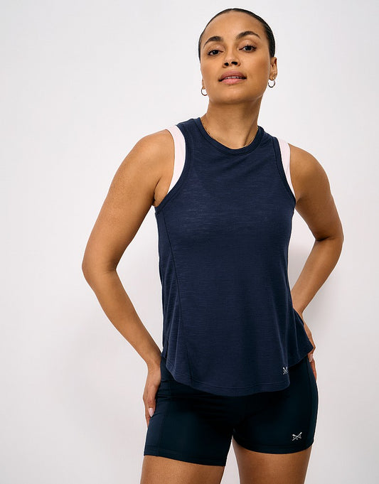 Front view of a woman wearing the dark navy blue Crew Clothing Lightweight Soft Slub Vest over a light pink crop top, paired with dark active shorts.