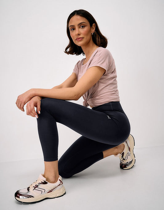 Side view of a woman crouching while wearing black Crew Clothing High Waisted 7/8 Leggings, paired with a light pink t-shirt and trainers.