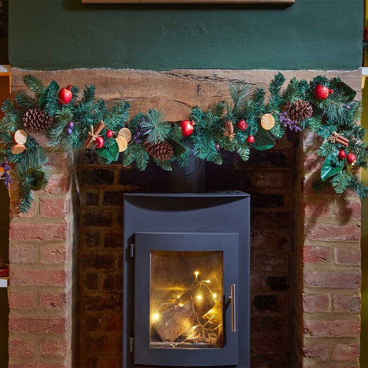 Smart Garden 180cm FestiveSpice garland decorated with pine cones, dried orange slices, and cinnamon sticks displayed over a fireplace mantel.