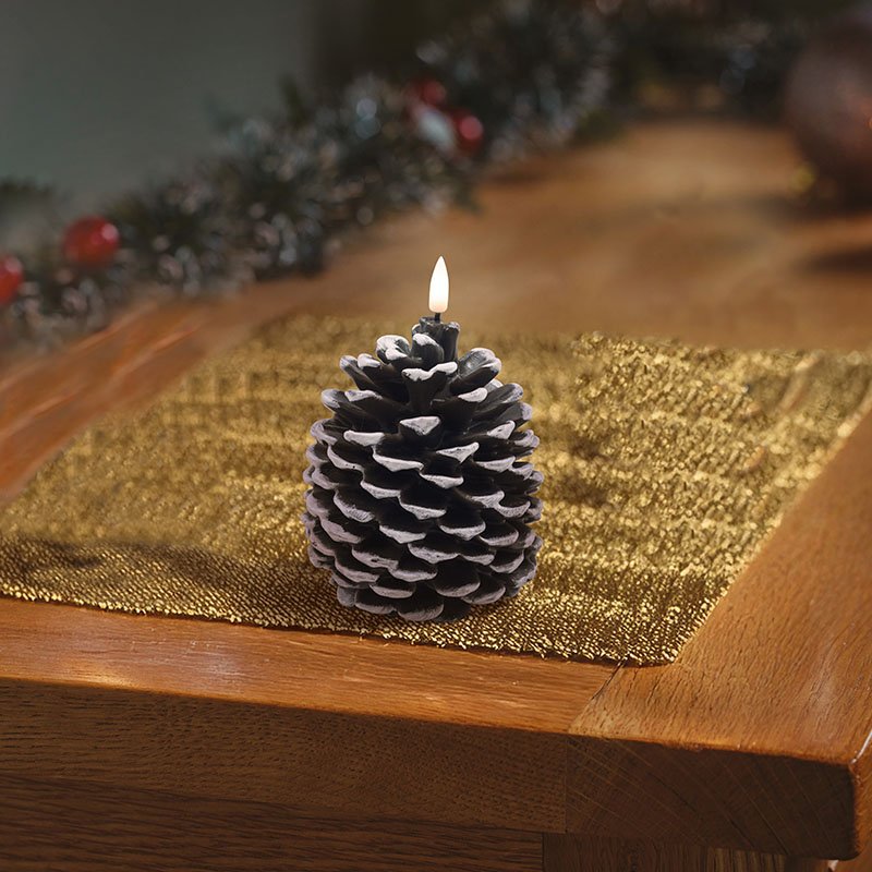 Smart Garden pinecone shaped LED wax candle glowing on a golden placemat on a wooden table.