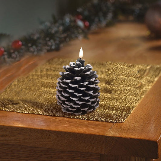Smart Garden pinecone shaped LED wax candle glowing on a golden placemat on a wooden table.