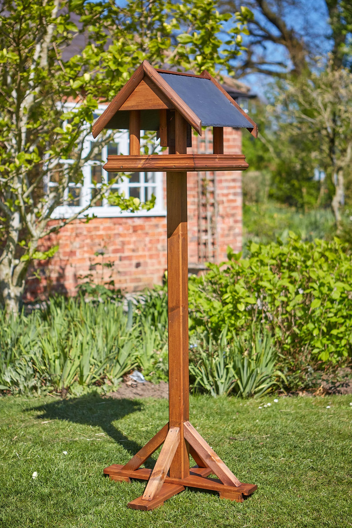Tom Chambers Sunbeam Bird Table with slate roof standing on a garden lawn.