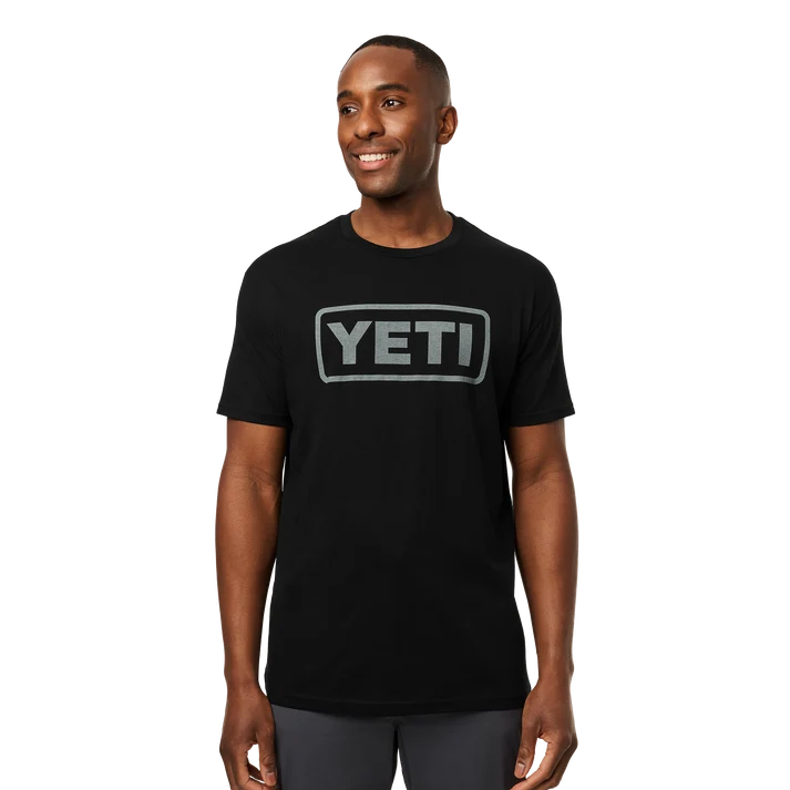 Men wearing YETI Full Logo Badge Short Sleeve T-Shirt in grey and black featuring front printed YETI badge logo